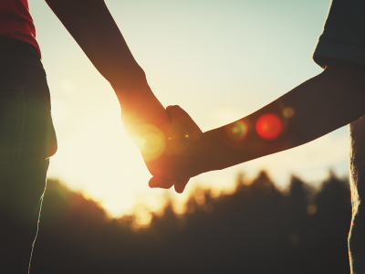 Silhouette of adult and child holding hands with sunrise in background